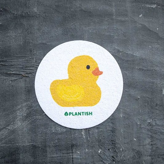 A white round kitchen sponge with a yellow duck print in the center, and the brand name 'PLANTISH' at the bottom.